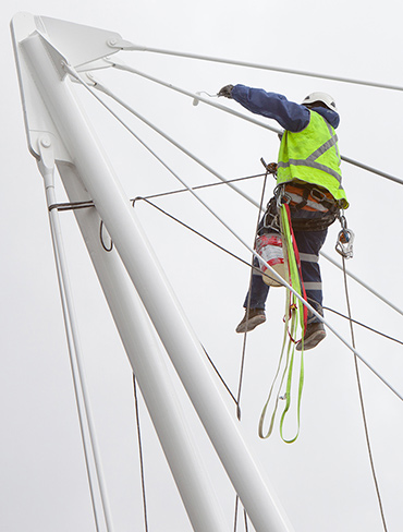 A technician tethered to a trapeze paints a bridge support.